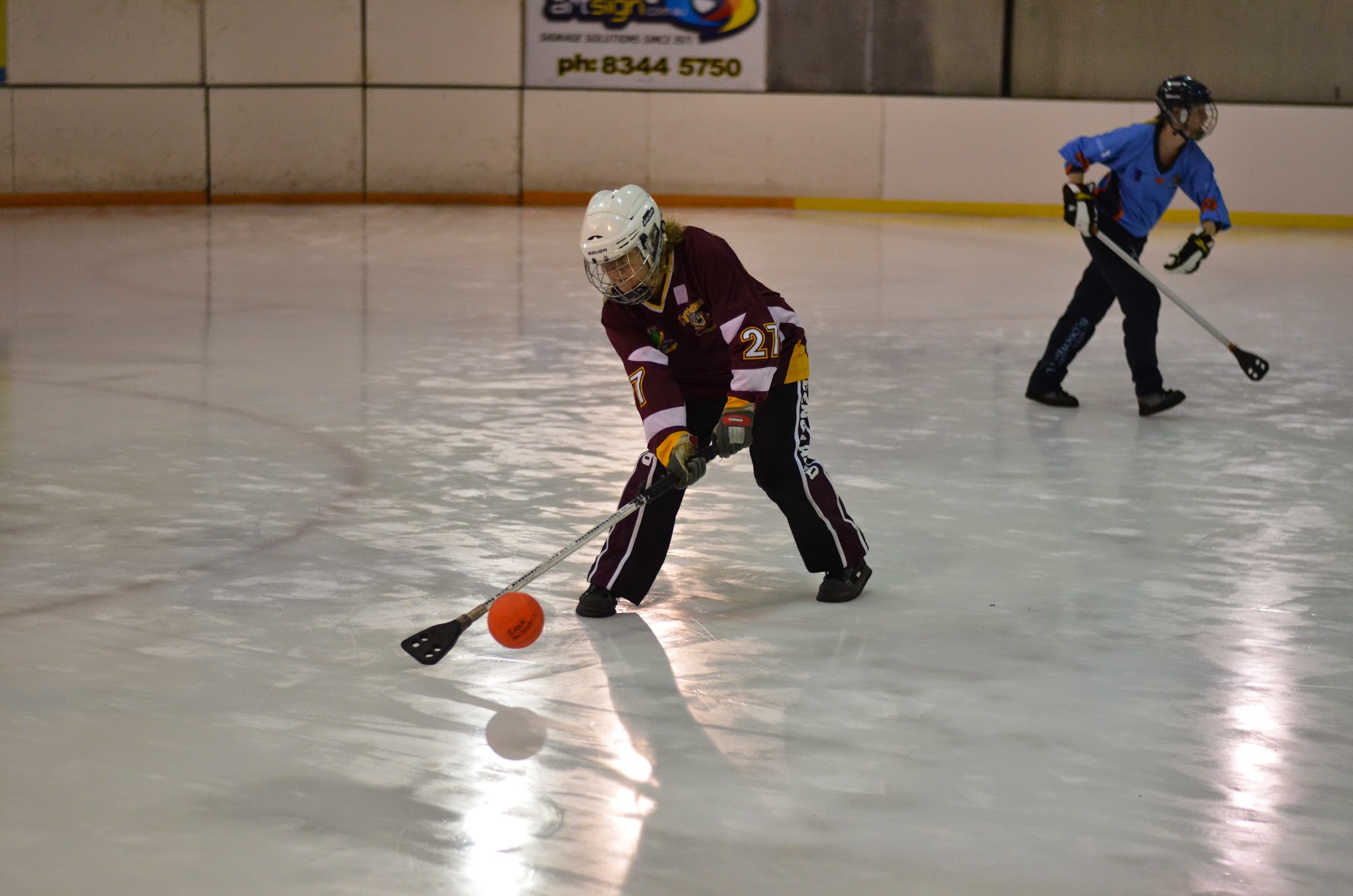 Player in maroon jersey striking the orange broomball